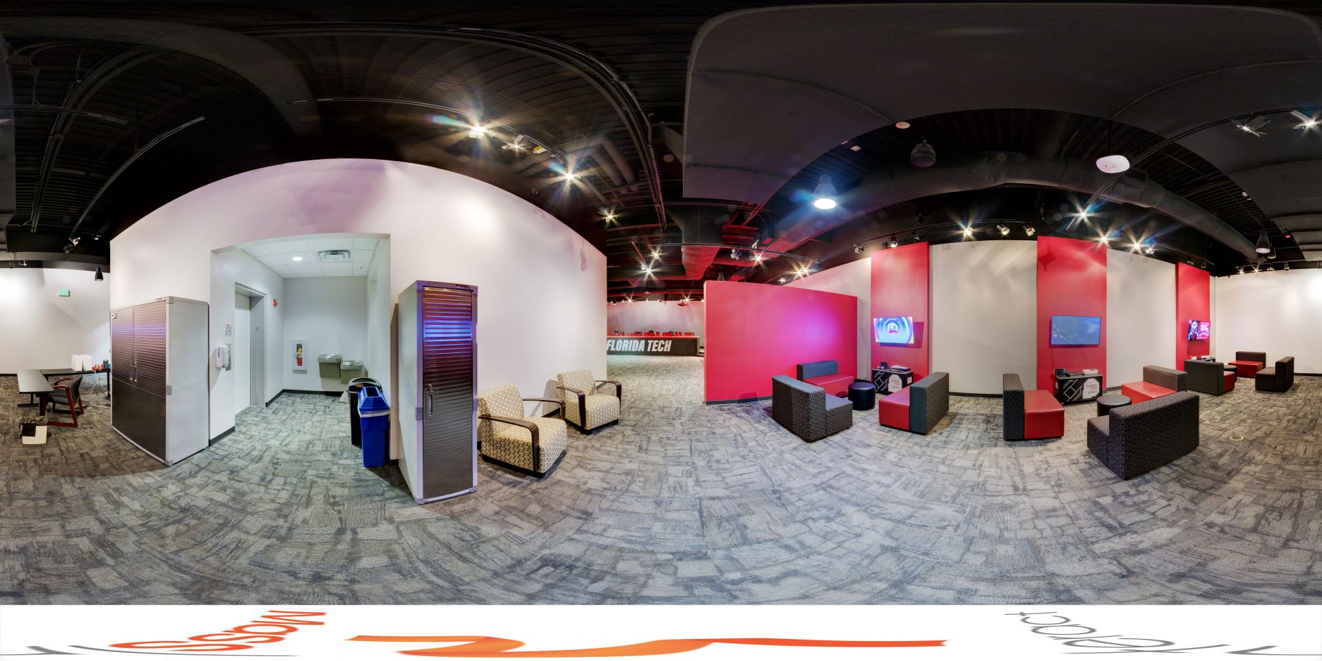 Panoramic view of the Esports center console area with gaming stations, consoles, and screens, featuring red and white walls and comfortable seating